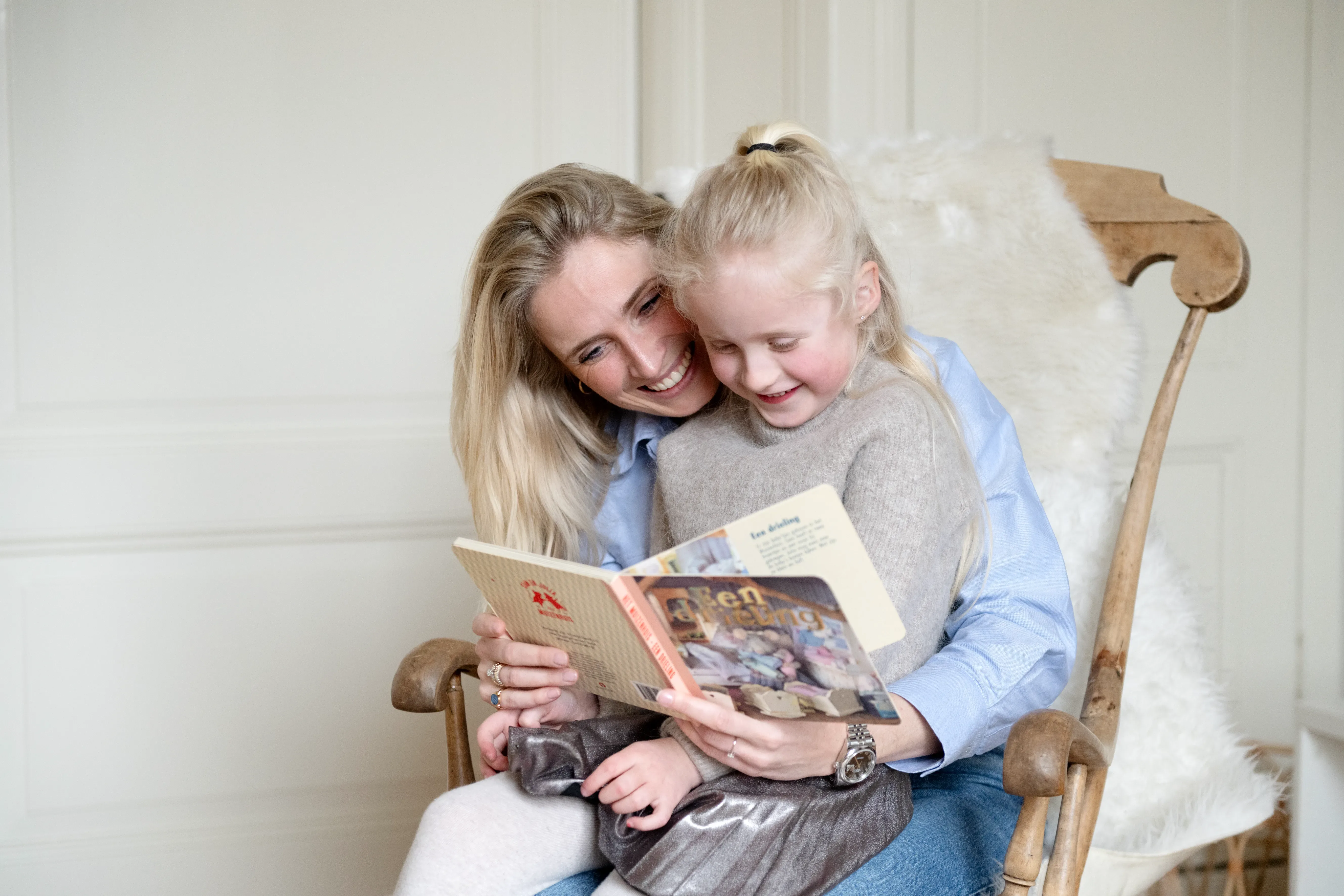 Vrouw met kind op schoot in wipstoel, een boek aan het lezen