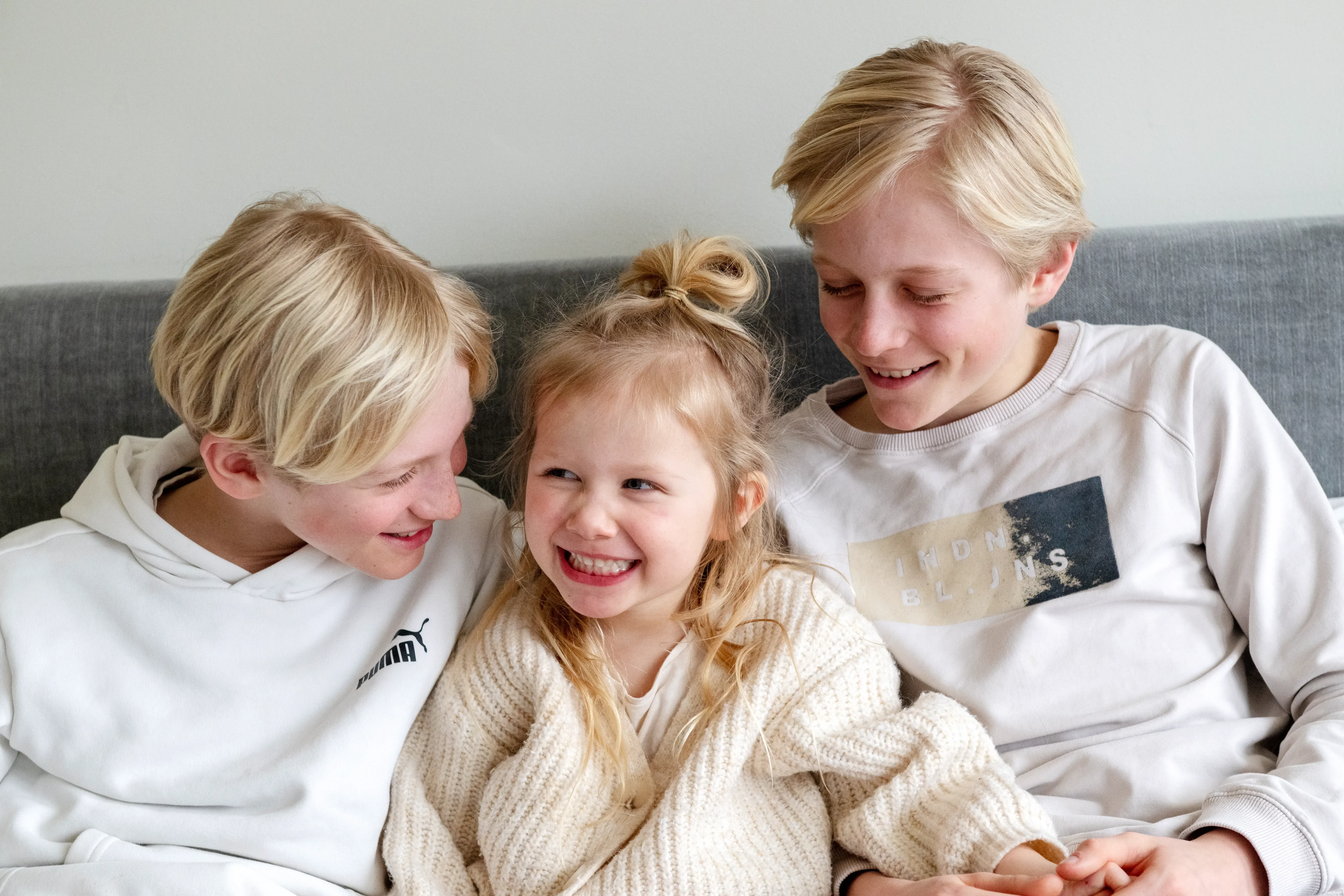 Drie kinderen zitten op bank en lachen naar elkaar