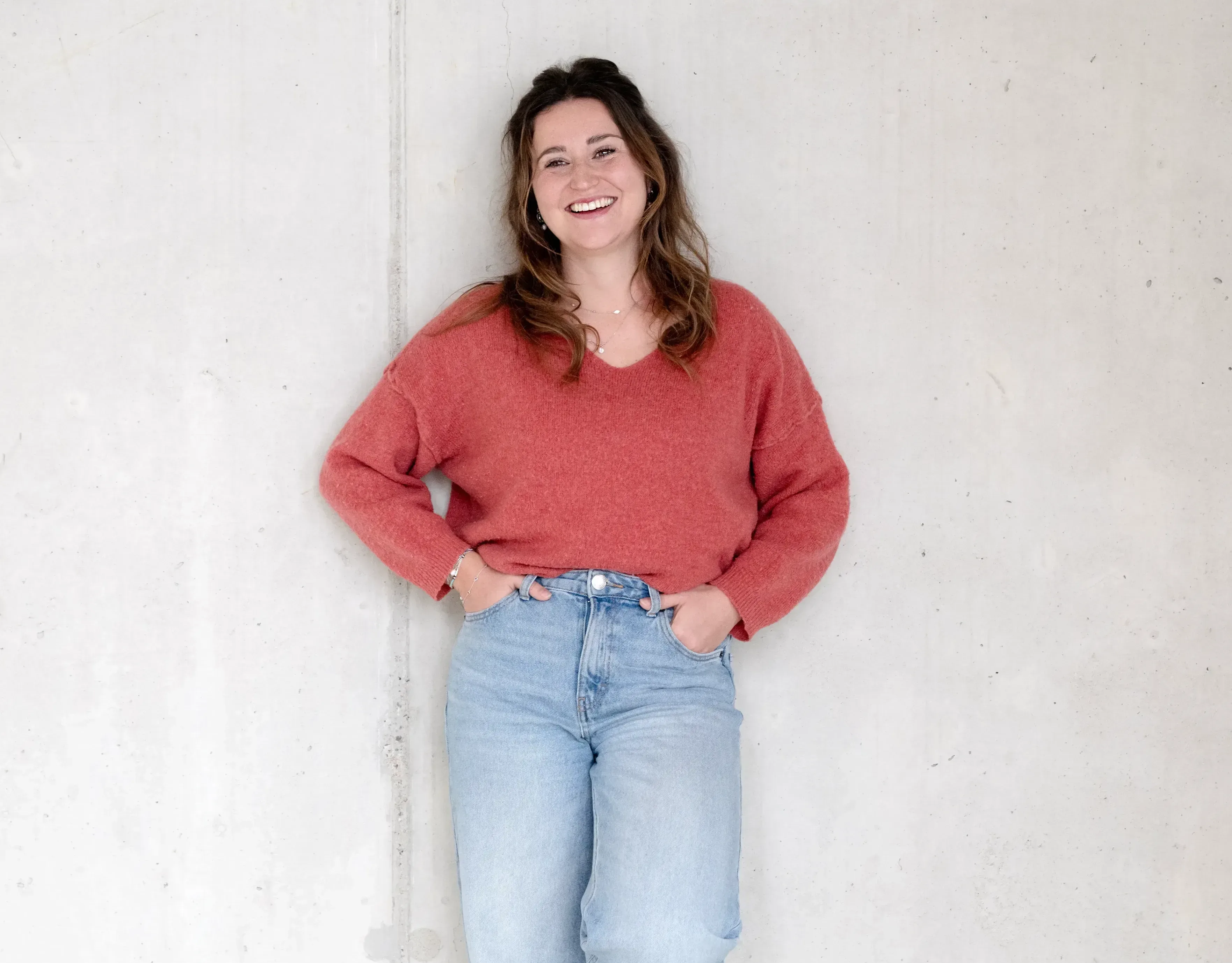 Vrouw tegen de muur aan het lachend naar de camera