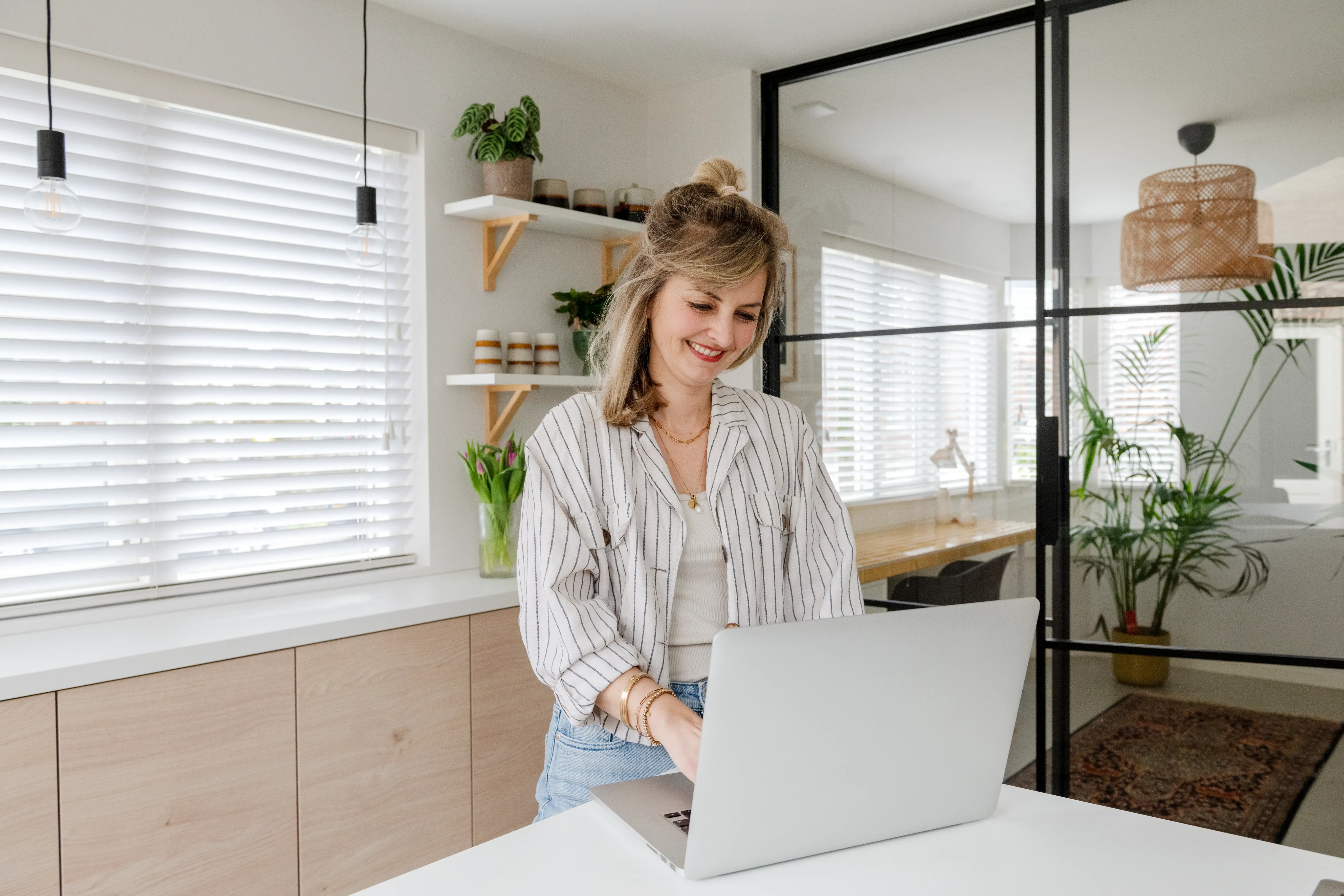 Vrouw staat achter keukentafel en kijkt naar laptop scherm