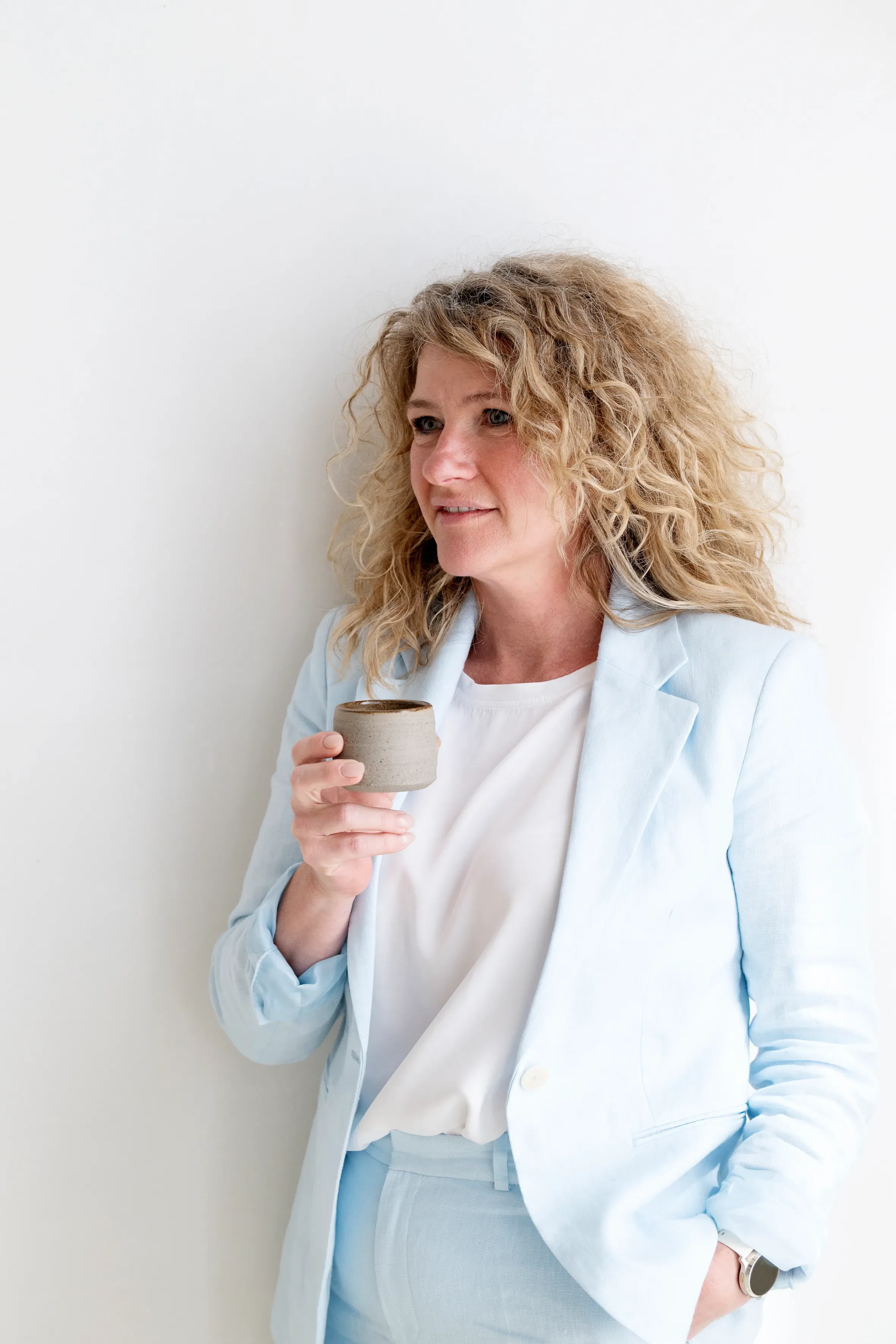 Vrouw leunend tegen muur met kopje in haar hand