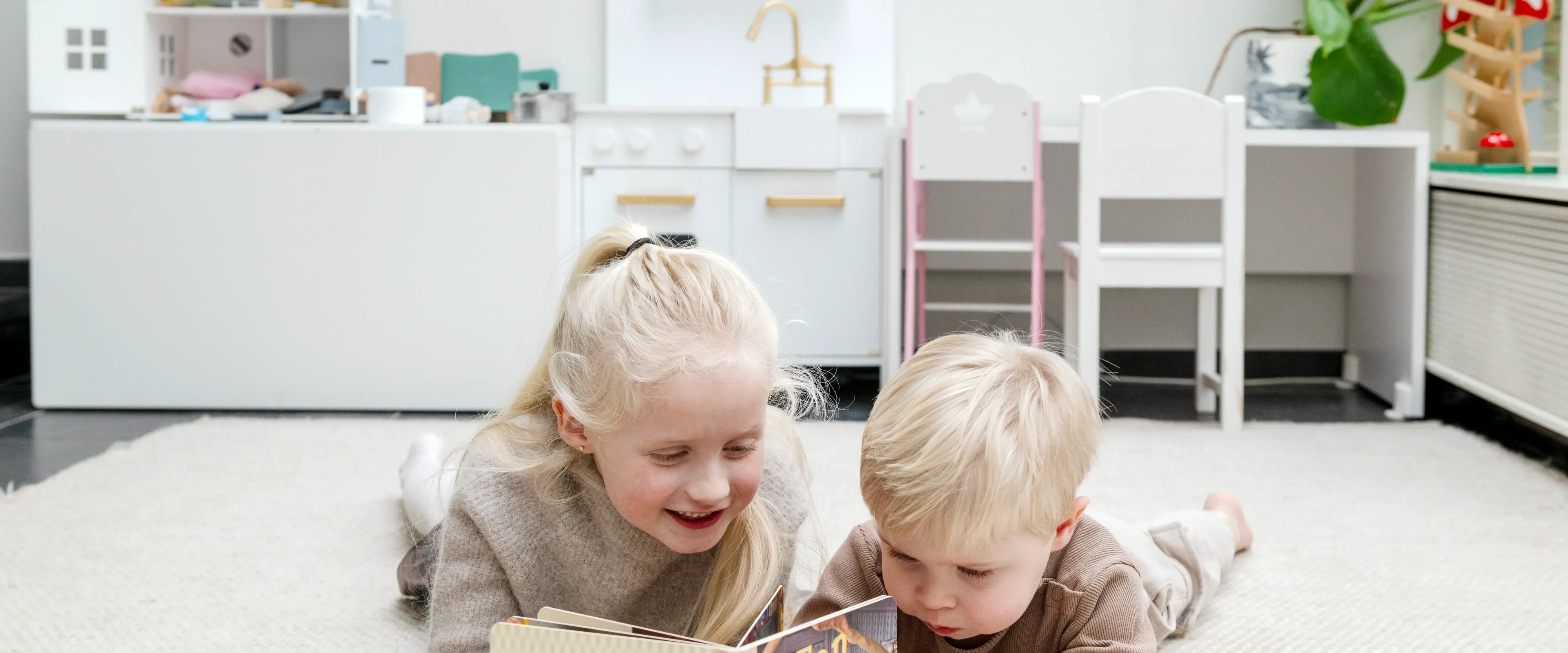 2 kinderen liggen op de grond en lezen boekje