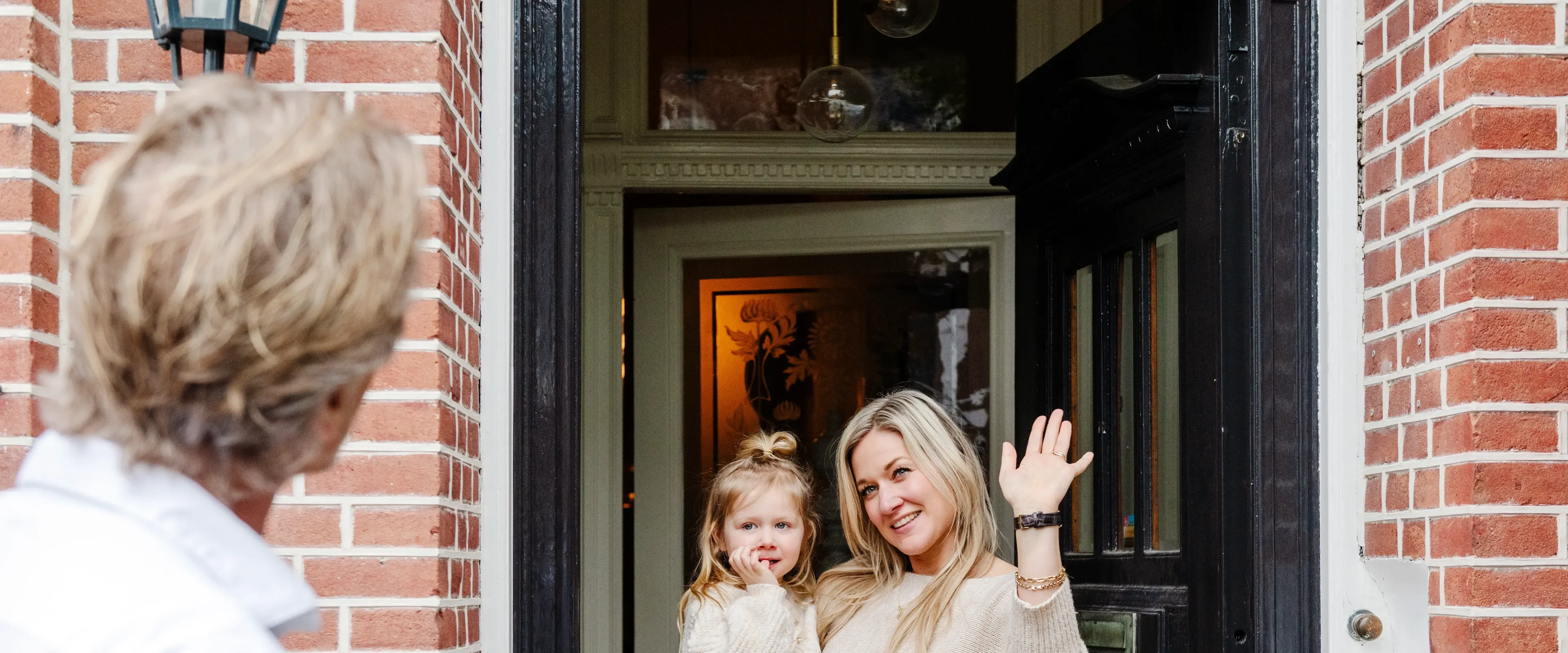 Vrouw met kind in haar armen, zwaaiend naar haar man