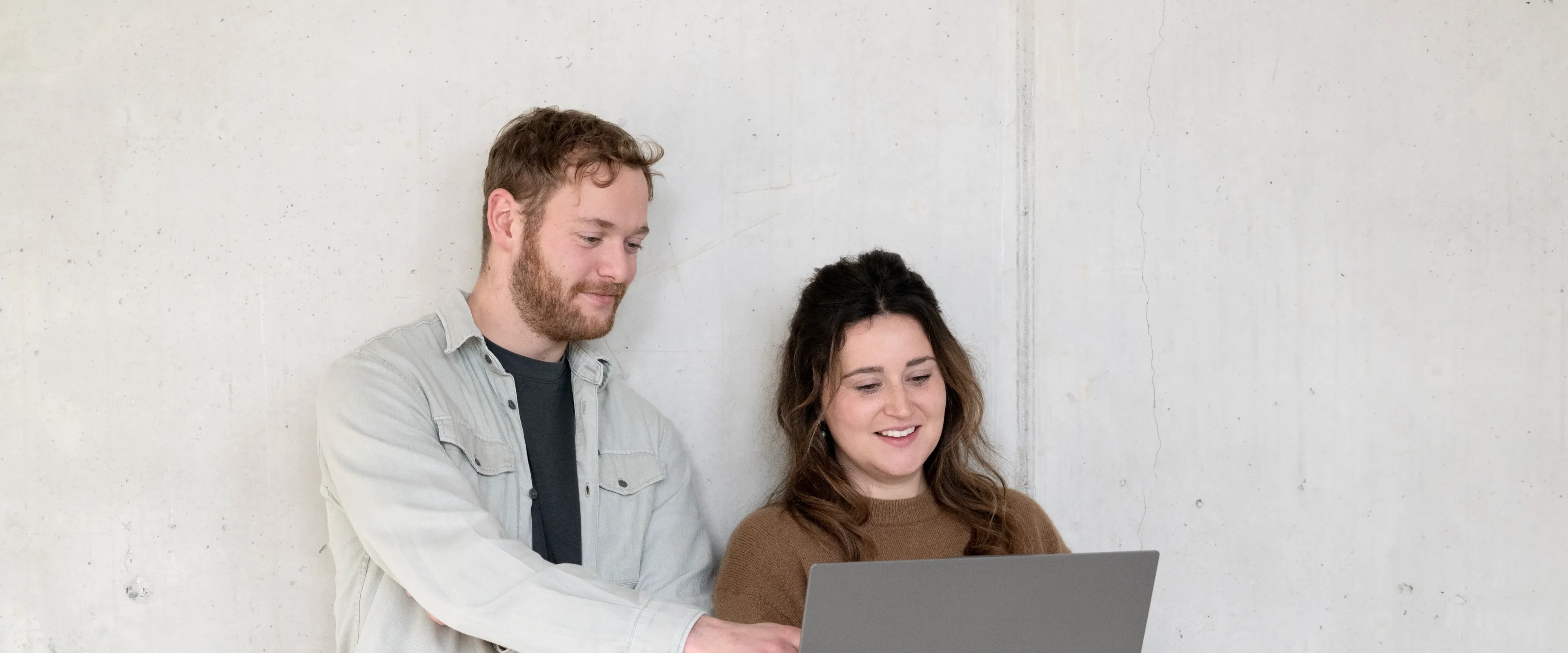 Man en vrouw leunend tegen muur kijken naar laptop