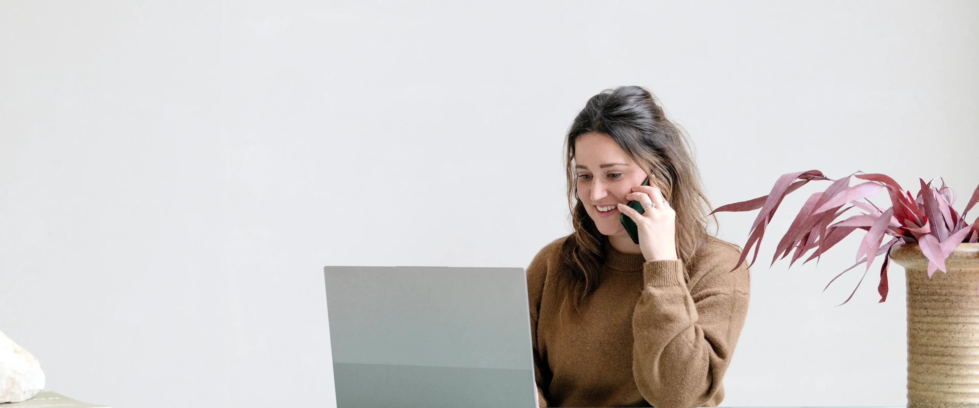 Vrouw aan tafel, bellend achter haar laptop