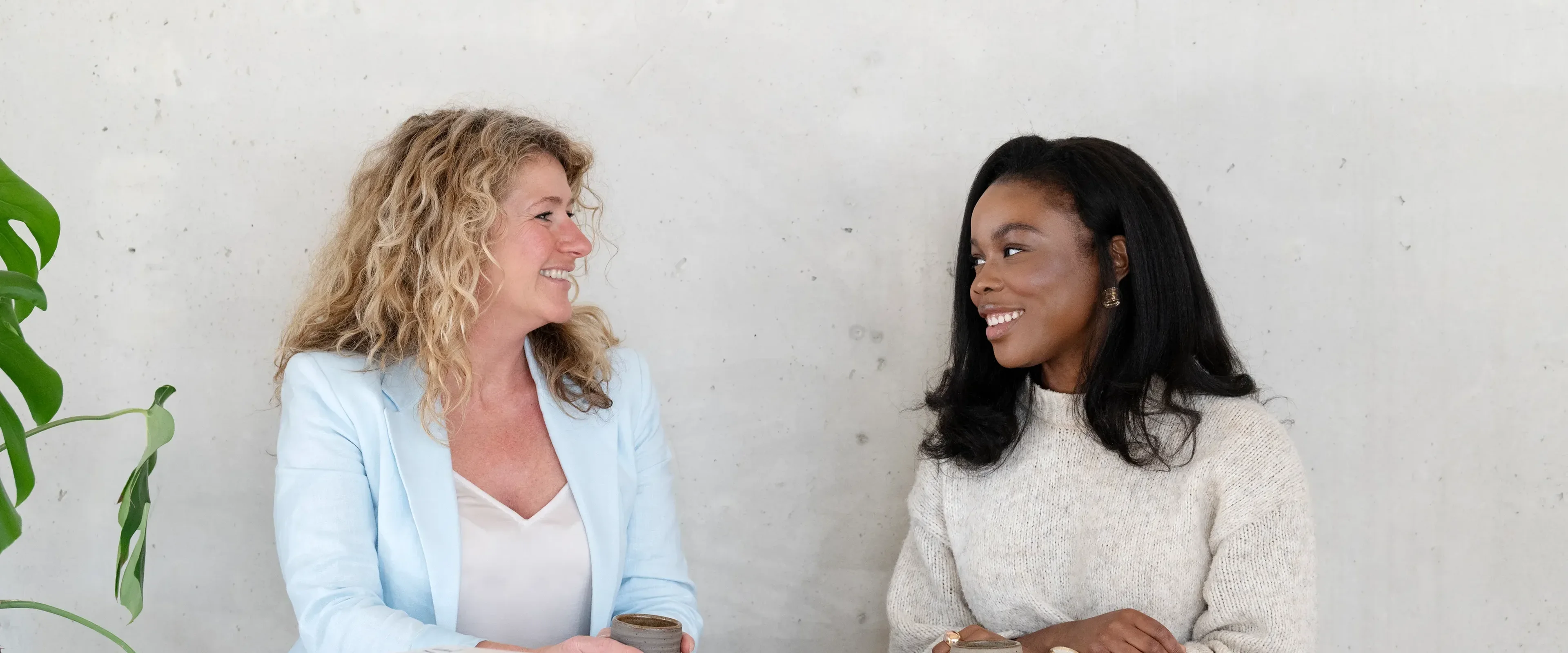 Twee vrouwen aan tafel glimlachend naar elkaar