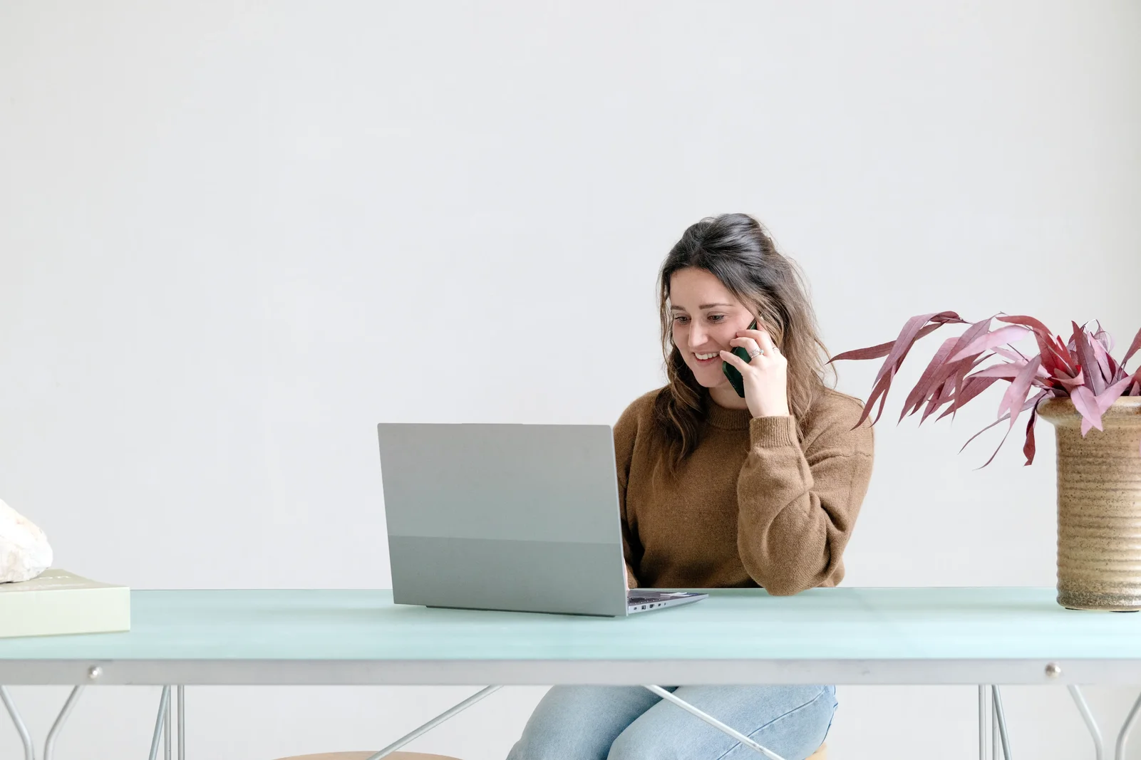 Vrouw aan tafel, bellend achter haar laptop