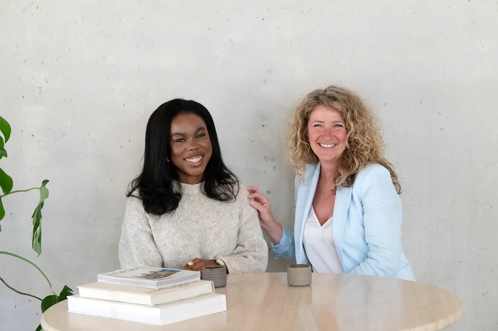2 vrouwen aan tafel lachend naar de camera