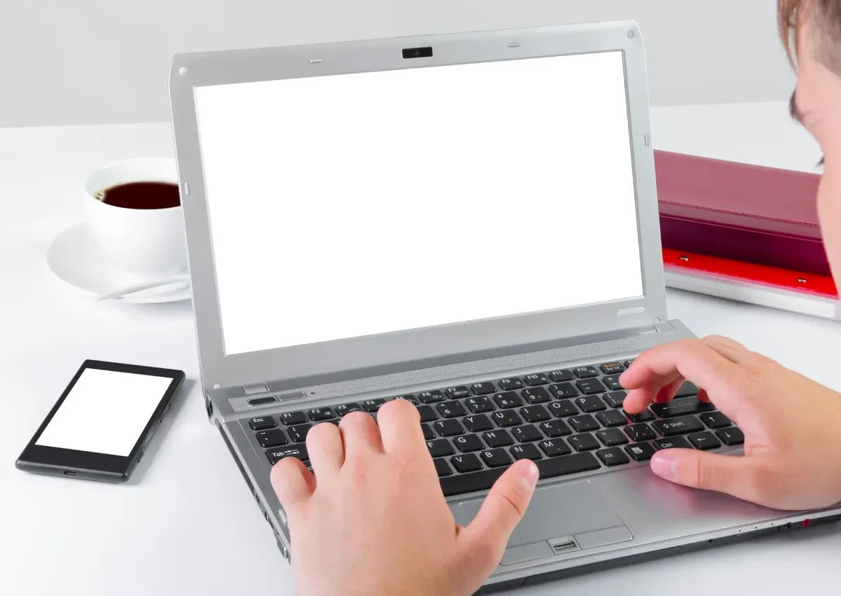 Persoon achter laptop aan het typen met telefoon naast laptop